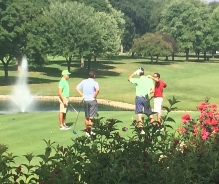 Image of four golfers talking on the Red Run Golf course standing near water with a fountain.