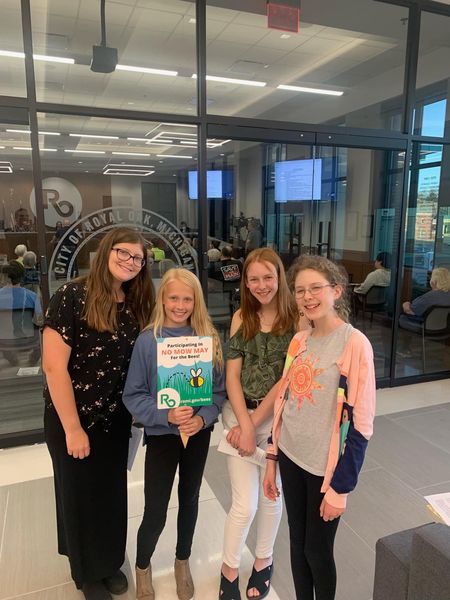 Members of the BeeTweens pose with No Mow May sign outside City Commission Chambers.